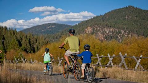 a family enjoys a mountain bike rental ride through the village at palisades tahoe on a sunny summer day