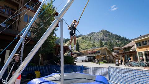 A kid enjoying the bungee trampoline at Palisades Tahoe with the mountains in the background.