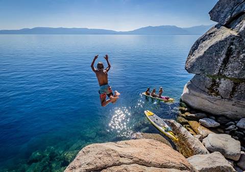 Boy jumping off rock into blue water at Lake Tahoe