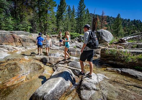 A group counselor guides campers safely across a flowing alpine creek in Olympic Valley