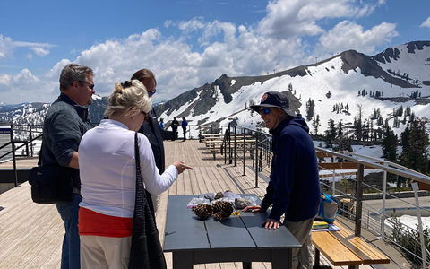 A naturalist stands in front of a table with objects, which they show to guests. Mountains are in the background.