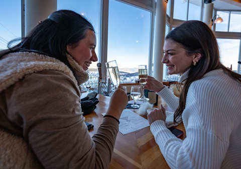 Two girls smiling and clinking glasses at Sunset Happy Hour