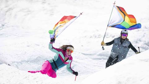 Two skiers carrying rainbow flags in a wiggle at Palisades Tahoe.