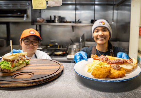 Two employees smiling and holding out plates of food at Rocker while working at Palisades Tahoe
