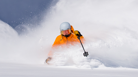 Skier in orange jacket making powder turn