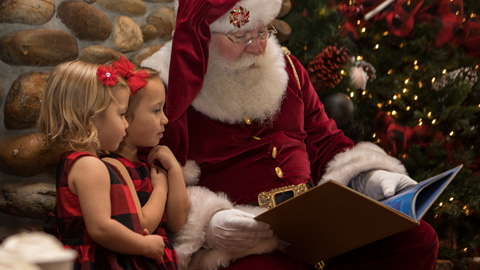 Two girls in Christmas dresses listening to a story read by Santa