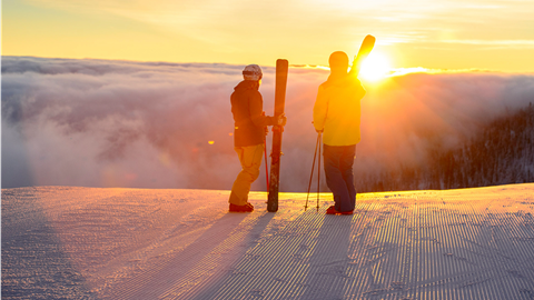 Two skiers looking over a sunrise with clouds
