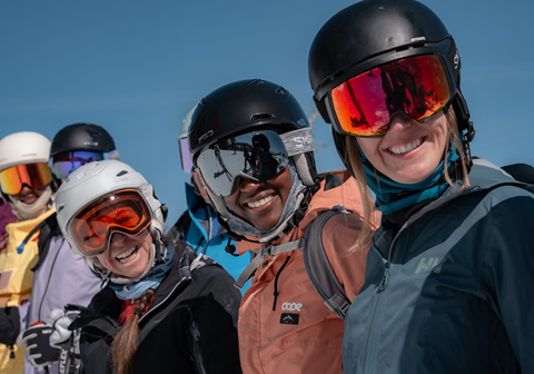 5 women smiling at a camera with ski googles and blue sky behind