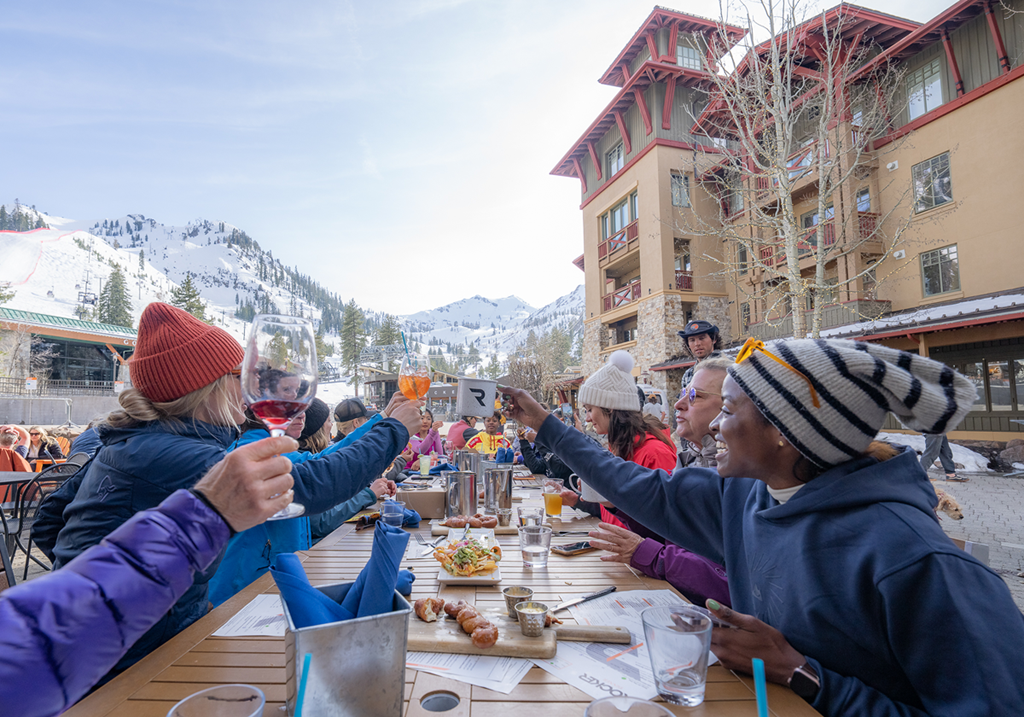 Group of gals clinking drinks while sitting outside at the Rocker patio