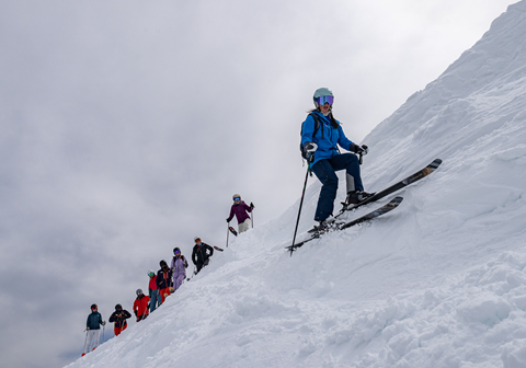 Skier in a blue jacket preparing to make a turn while a group watches