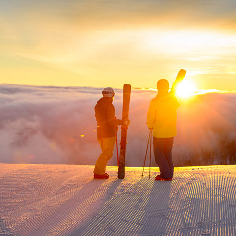 Scenic view of skiers looking out at a sunrise over a groomed run