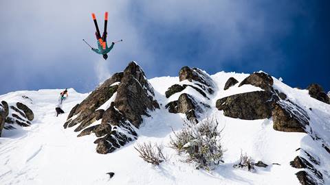 A skier does a backflip while a photographer takes a picture right behind them. 