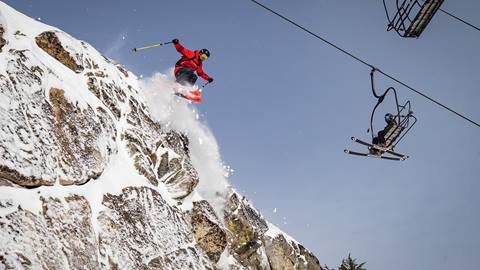 A skier hucks a cliff off Granite Chief while riders of the chairlift watch in the background.