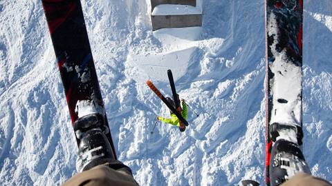 A skier on the chairlift takes a photo of a backflip happening right beneath him. 
