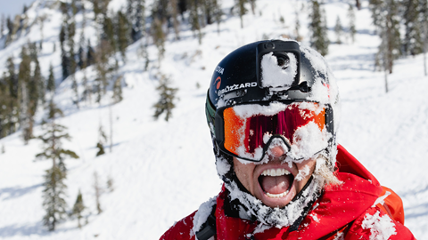 Skier smiling at camera with wide grin and snow on googles