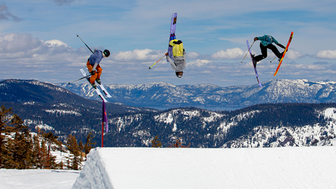 Three skiers throw tricks off of a jump in the terrain park. 