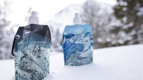 Two reusable branded water bottles sitting on snow. 