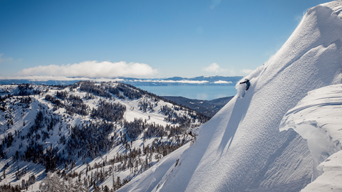 A snowboarder slashes through powder on a bluebird day with a view of Lake Tahoe