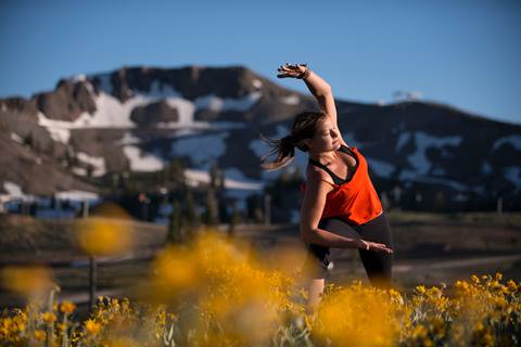 A woman poses yoga-style in front of snow-capped mountains. 