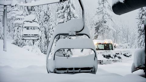 Chairlift with feet of snow and a grooming machine at Palisades Tahoe