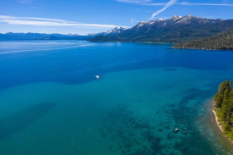 An aerial picture of Lake Tahoe, with a white boat in the center and evergreen trees on the shoreline. 