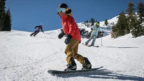 A snowboarder and 2 skiers riding a groomer at Alpine Meadows on a sunny spring day