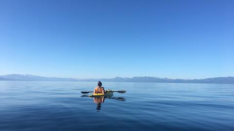 A kayaker floats on the glassy summer waters of Lake Tahoe