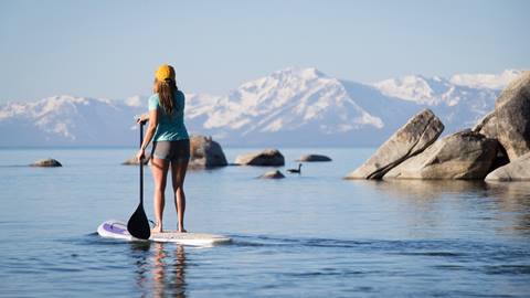 Woman paddle boarding on Lake Tahoe with the Sierra Nevada mountains in the background