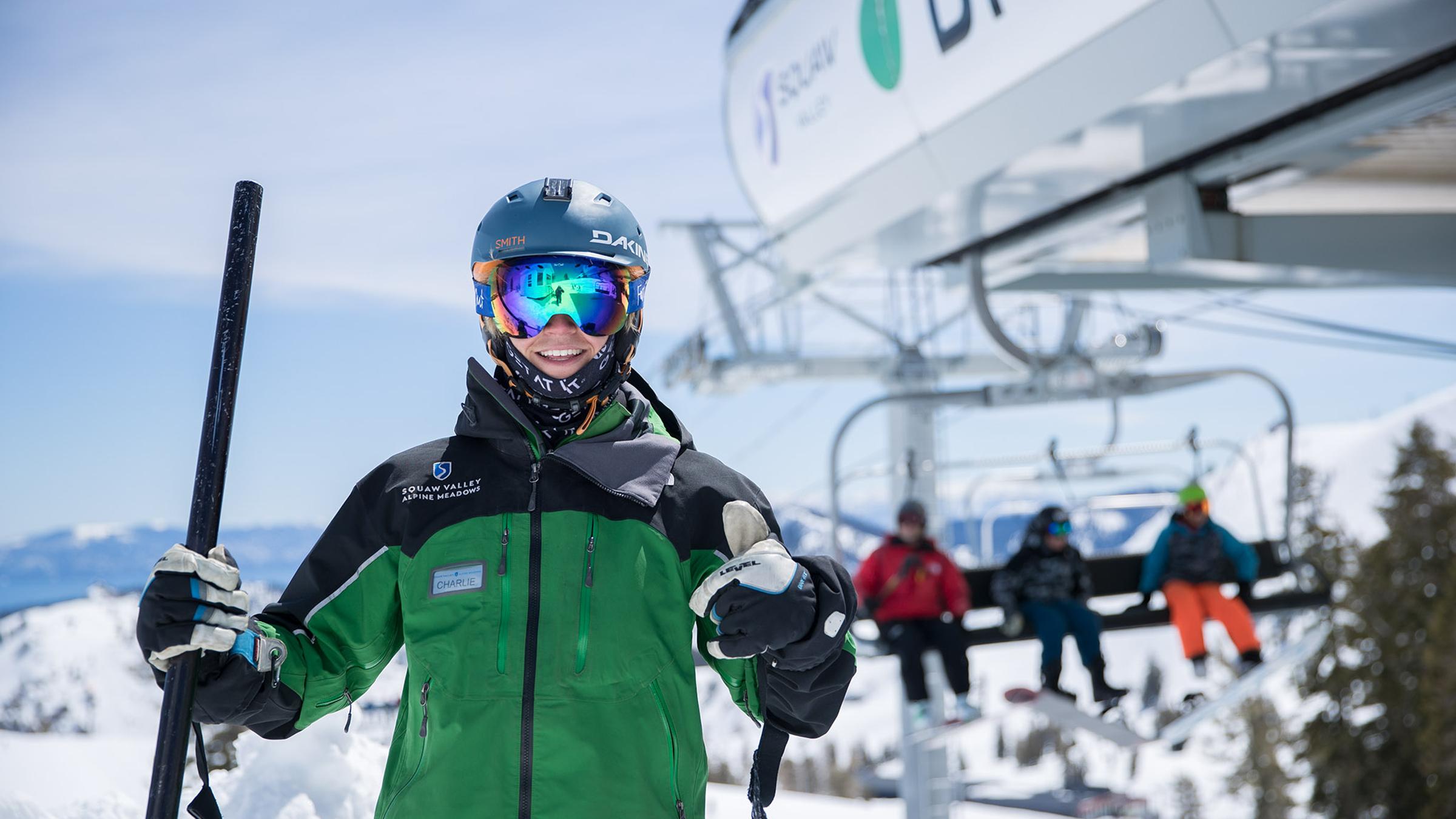 A lift attendant at the top of Big Blue giving a thumbs up with group unloading a chairlift in the background
