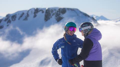 A female instructor interacting with her student with Palisades in the background at Ski & Snowboard School at Squaw Valley