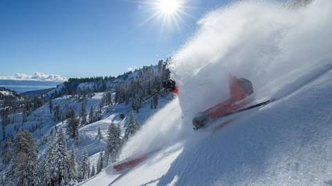 A skier making a powder turn in deep snow at Alpine with Lake Tahoe in the background