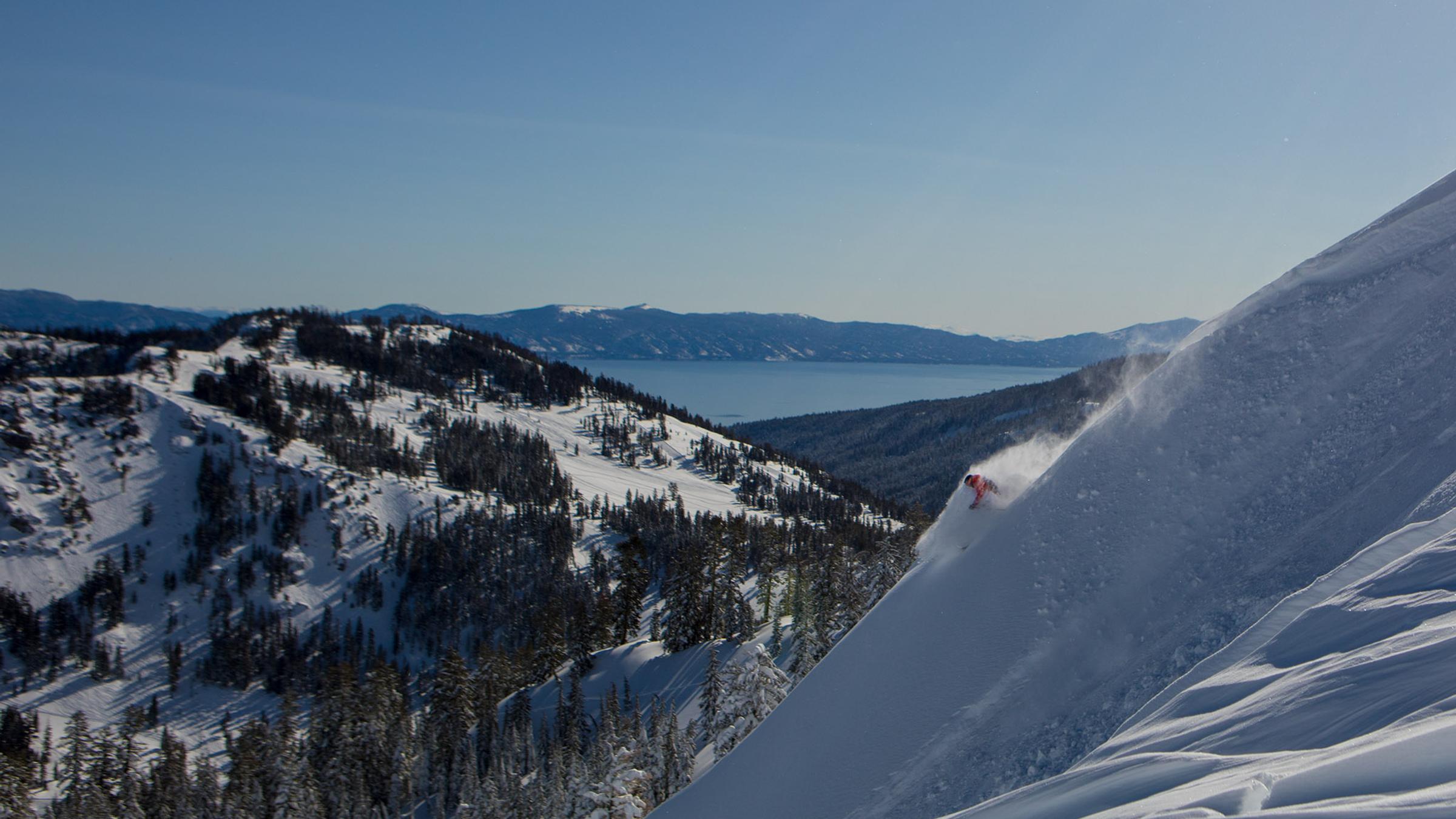 A skier skiing deep powder on a ridge line at Alpine Meadows with Lake Tahoe in the background